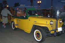 Cool vintage Willys Jeepster towing a small trailer full of carved tikis for sale at the beach in Huntington 
