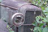 Radiator shell and original headlamp on Ford pickup truck in classic car salvage yard